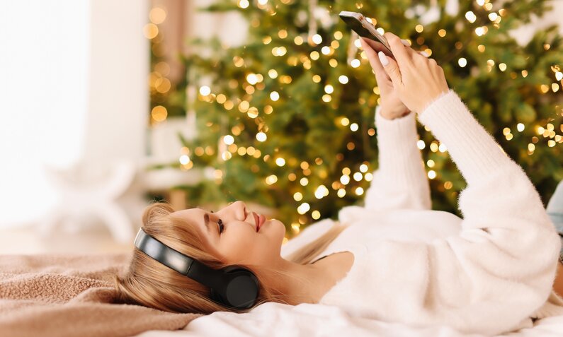 Frau hört Musik mit Kopfhörern vom Weihnachtsbaum | ©  Getty Images / Elizaveta Starkova