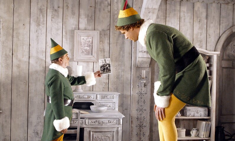 Bob Newhart und Will Ferrell stehen sich in einer Szene des Kinofilms "Buddy - Der Weihnachtself" in grünen Elfenkostümen in einem Zimmer mit grauen Holzwänden gegenüber, Newhart zeit Ferrell ein Foto | © ddp images