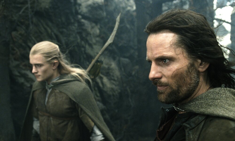Orlando Bloom und Viggo Mortensen eilen in einer Szene aus dem KInofilm "Der Herr der Ringe - Die Rückkehr des Königs" in Elbengewändern durch den Wald. | © ddp images/mptv
