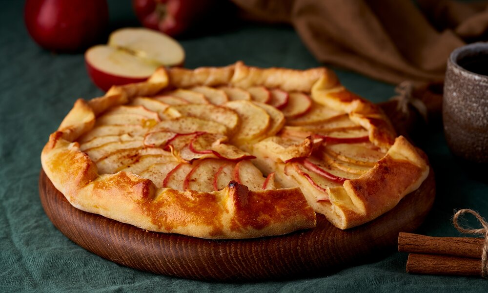Apfel-Tarte in Nahaufnahme neben Apfel liegend. | © Getty Images / NataBene