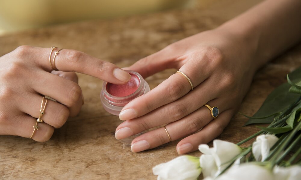 Frauenhände mit Ringen, tragen rosa Creme aus Döschen auf. | © Getty Images / 	JGI/Jamie Grill