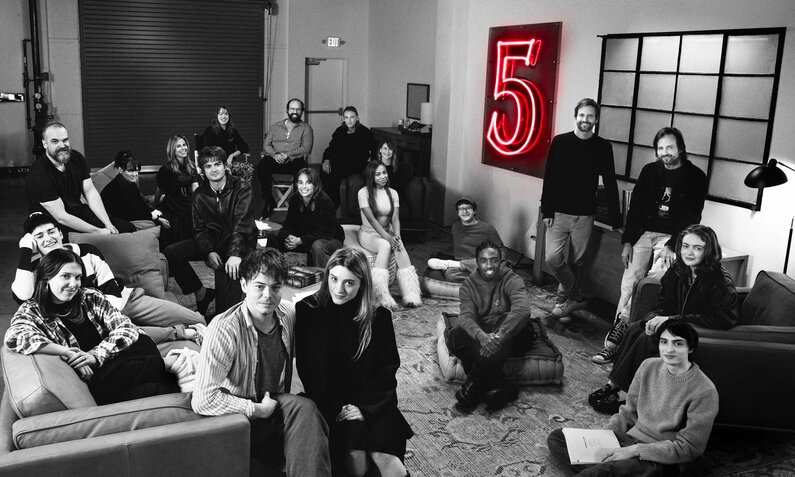 Cast und Crew der Netflix-Serie "Stranger Things" sitzen auf einem Schwarz-Weiß-Foto in einem Raum bei Produktonsstart - an der Wand leuchtet die Ziffer 5 | © Netflix