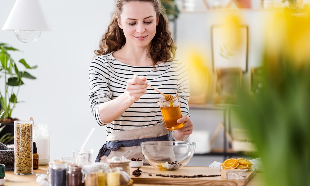 Frau in gestreiften Oberteil gibt einen Löffel Honig über ihr Essen. | © Getty Images / KatarzynaBialasiewicz