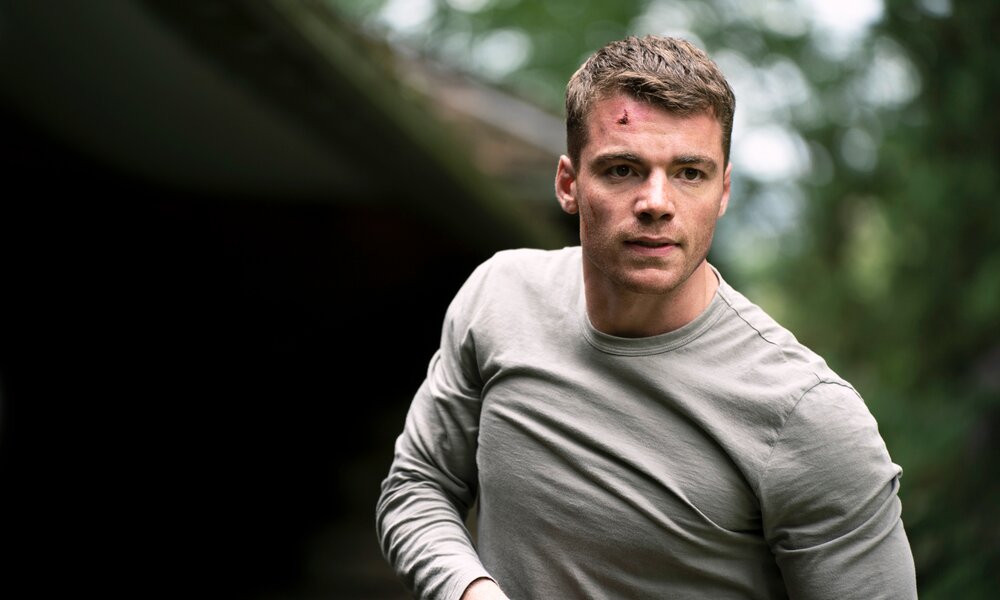 Gabriel Basso im grauen Shirt vor dunklem Hintergrund in einer Szene aus der Netflix-Serie "The Night Agent"  | © Netflix/Dan Power
