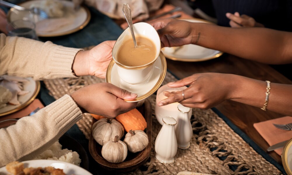 Mehrere Hände am gedeckten Tisch reichen sich Sauce in Behälter. | © Getty Images / Martine Severin