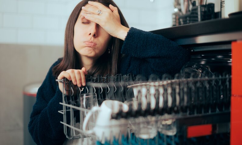 Frau sitzt vor Spülmaschine und schlägt die Hände vorm Kopf zusammen | ©  Shutterstock/ Nicoleta Ionescu