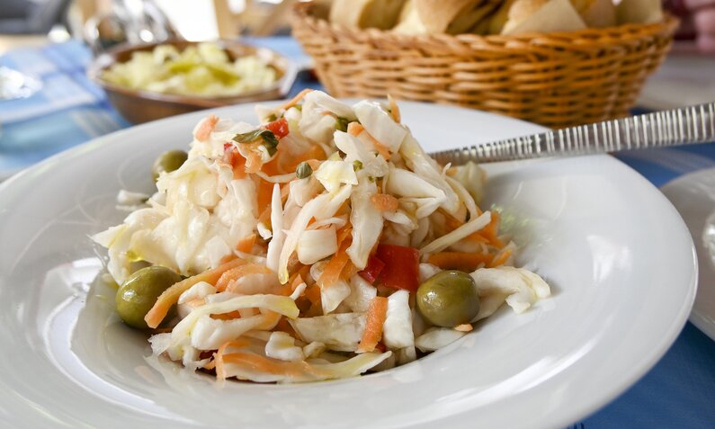 Griechischer Krautsalat mit Oliven angerichtet auf einem weißen Teller in einem Restaurant. | © Getty Images / ConstantinosZ