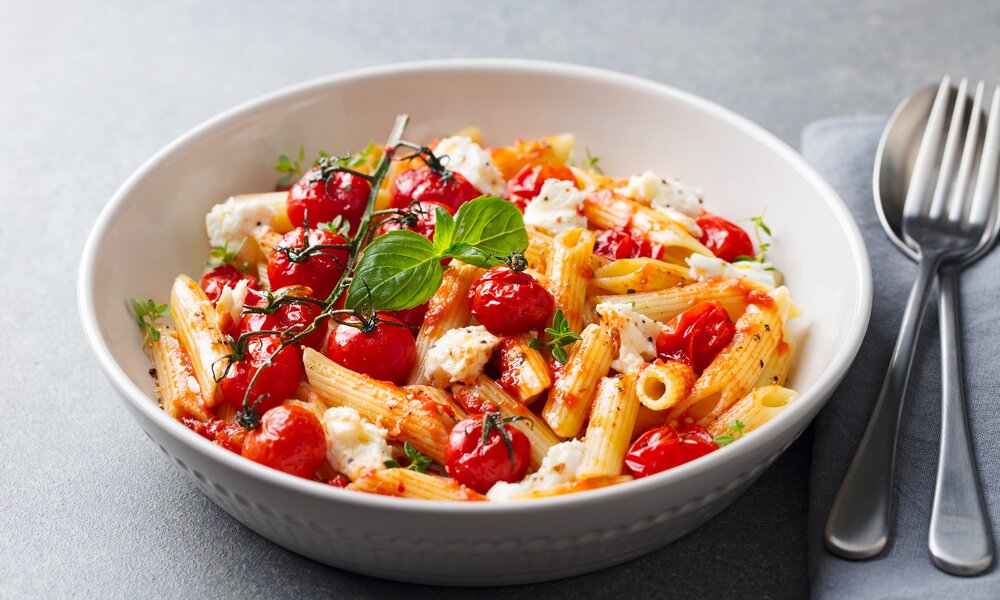 Penne mit Cherry-Tomaten und kleinen Mozzarella-Kugeln angerichtet in einer weißen Schale.  | © Getty Images / 	AnnaPustynnikova