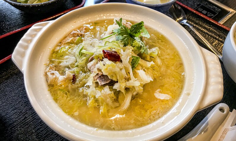 Sauerkraut in Suppe, mit Speckwürfeln garniert, angerichtet in weißem Suppenteller. | © Getty Images / DigiPub