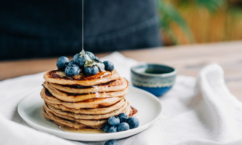 Gestapelte Pancakes auf einem Teller, garniert mit Blaubeeren. | © Getty Images / Maria Korneeva