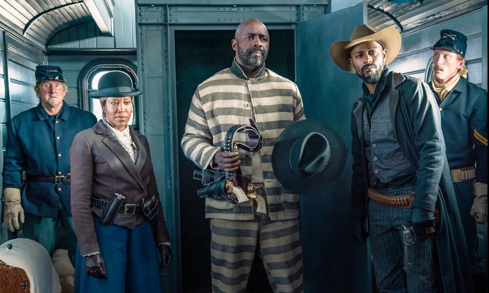 Regina King, Idris Elba Rufus Buck und Lakeith Stanfield stehen in einer Szene des Netflix-Western "The Harder They Fall" umrahmt von zwei Polizisten in einemaltmodischen Zugwaggon. | © Netflix/David Lee