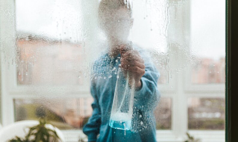 Frau sprüht mit Glasreiniger auf Fenster | ©  Getty Images/ Carol Yepes