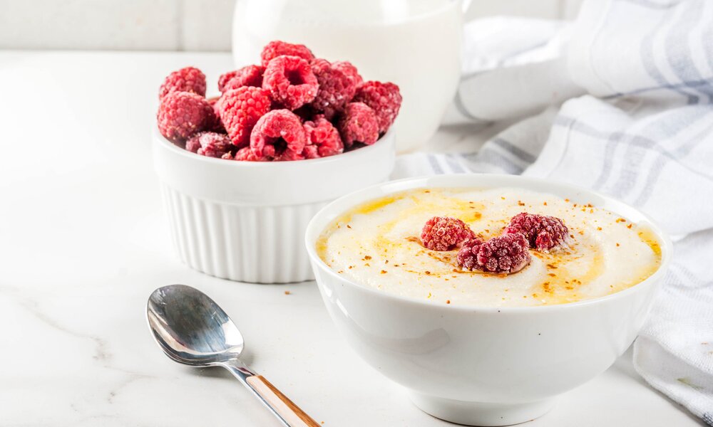 Griesbrei garniert mit Himbeeren in weißer Schüssel. | © Getty Images / Rimma_Bondarenko