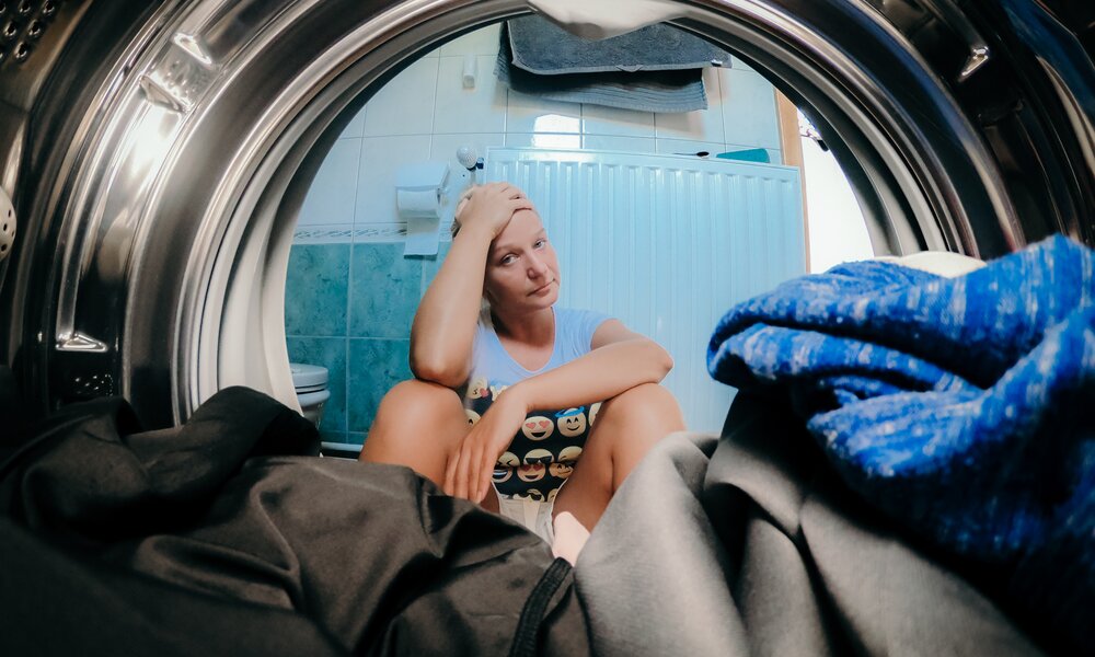 Verärgerte Frau, die Kleidung in Waschmaschine im Badezimmer anschaut | ©  Getty Images/ SimonSkafar