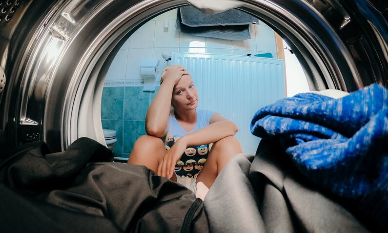 Verärgerte Frau, die Kleidung in Waschmaschine im Badezimmer anschaut | ©  Getty Images/ SimonSkafar