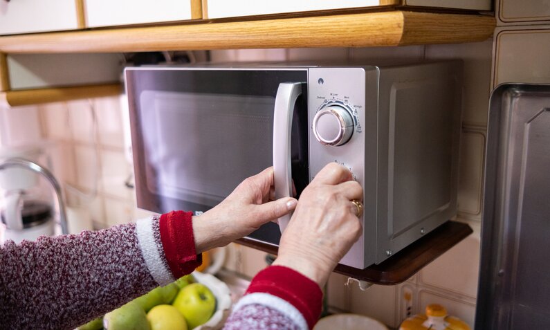 Frau wärmt Essen in der Mikrowelle auf | ©  Getty Images/ Alavinphoto