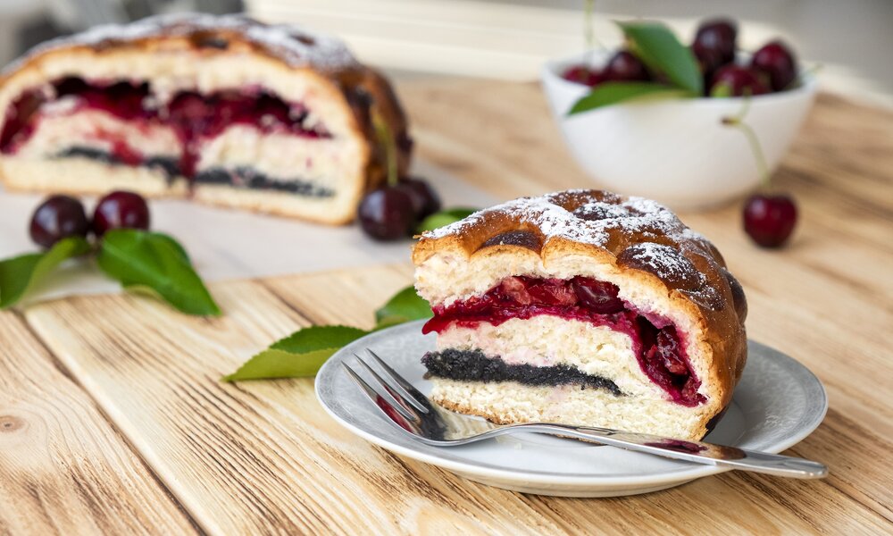 Kuchenschnitt, angeschnitten mit Füllung aus Kirschen und Mohn, angerichtet auf Holzuntergrund. | © Getty Images / Nemer-T
