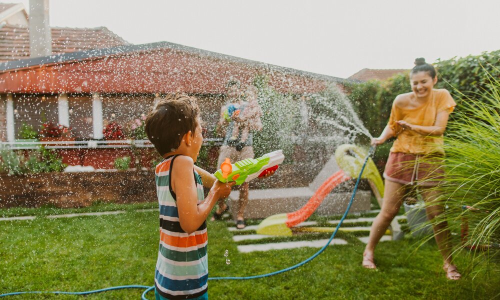 Frau und Kinder machen Wasserschlacht im Garten | ©  Getty Images/ AleksandarNakic