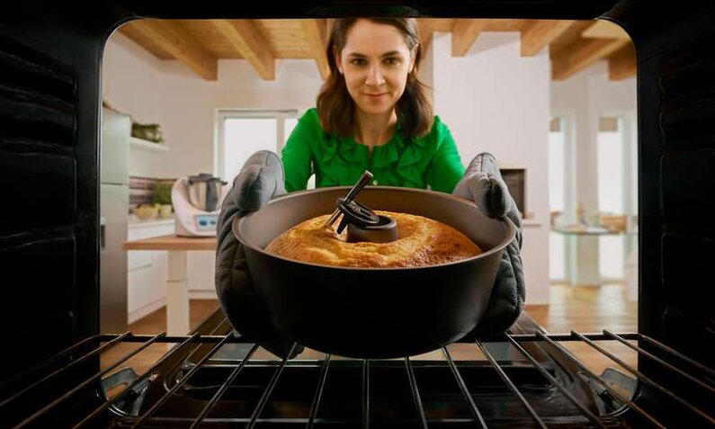 Frau schiebt Kuchen mit Thermomix-Sensor in den Backofen, Sicht aus dem Ofen heraus. | © Vorwerk