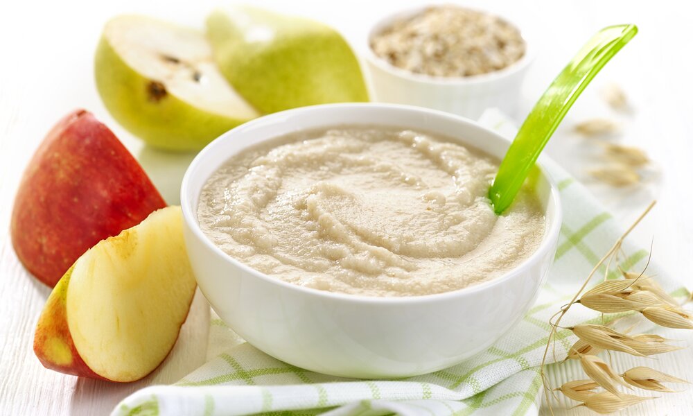 Brei in Keramikschüssel, darin ein Babylöffel, dahinter ein Apfel. | © Getty Images / 	Magone
