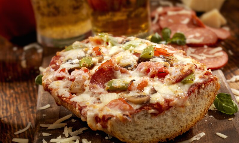 Aufgeschnittene und belegte Pizza-Baguette, belegt mit Salami, Paprika und Käse, auf rustikalem Holzuntergrund. | © Getty Images / LauriPatterson