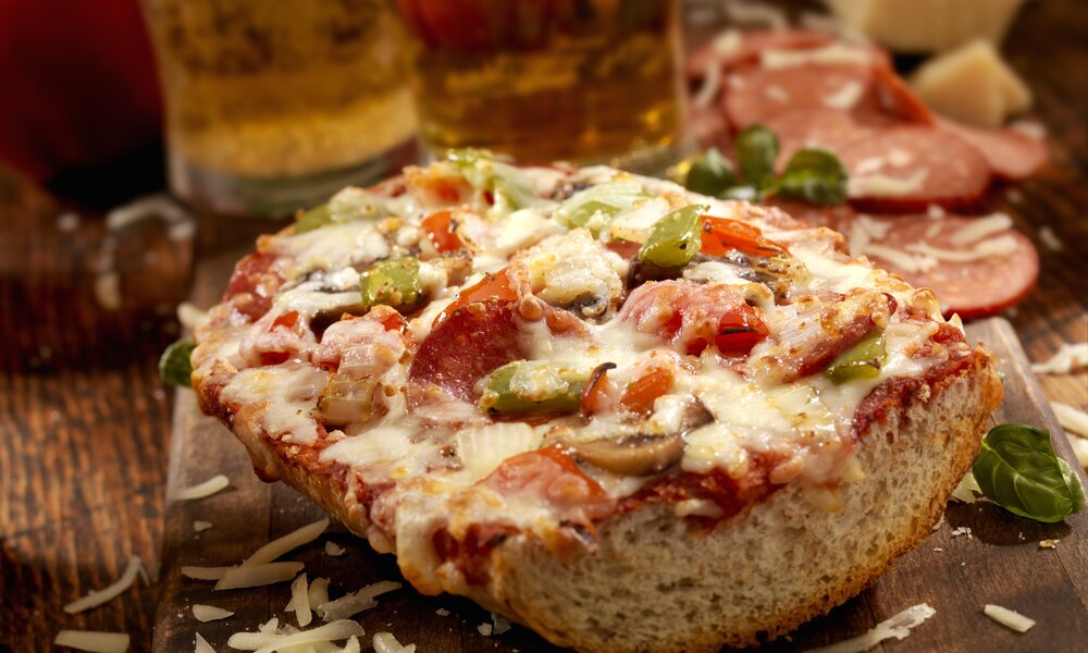 Aufgeschnittene und belegte Pizza-Baguette, belegt mit Salami, Paprika und Käse, auf rustikalem Holzuntergrund. | © Getty Images / LauriPatterson