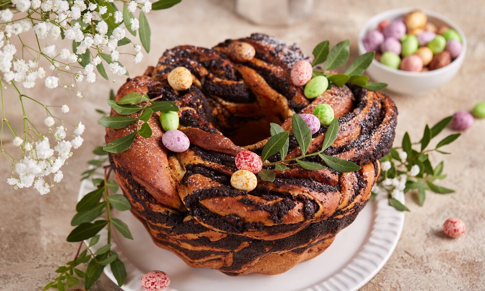 Osterkranz mit Mohnfüllung, dekoriert mit frischen Zweigen, angerichtet auf einem Mamoruntergrund. | © Getty Images / 	Natkinzu