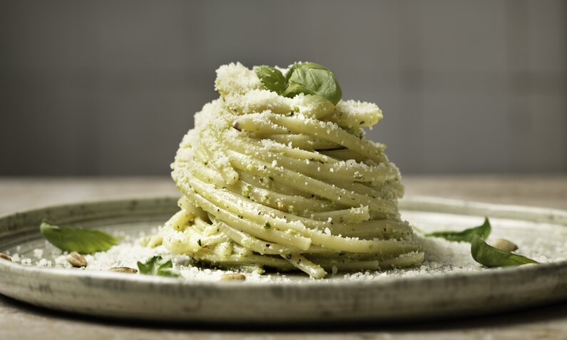 Spaghetti mit Basilikum und Parmesan bestreut, aufgedreht auf einem weißen Teller. | © Getty Images / 	Monica Bertolazzi