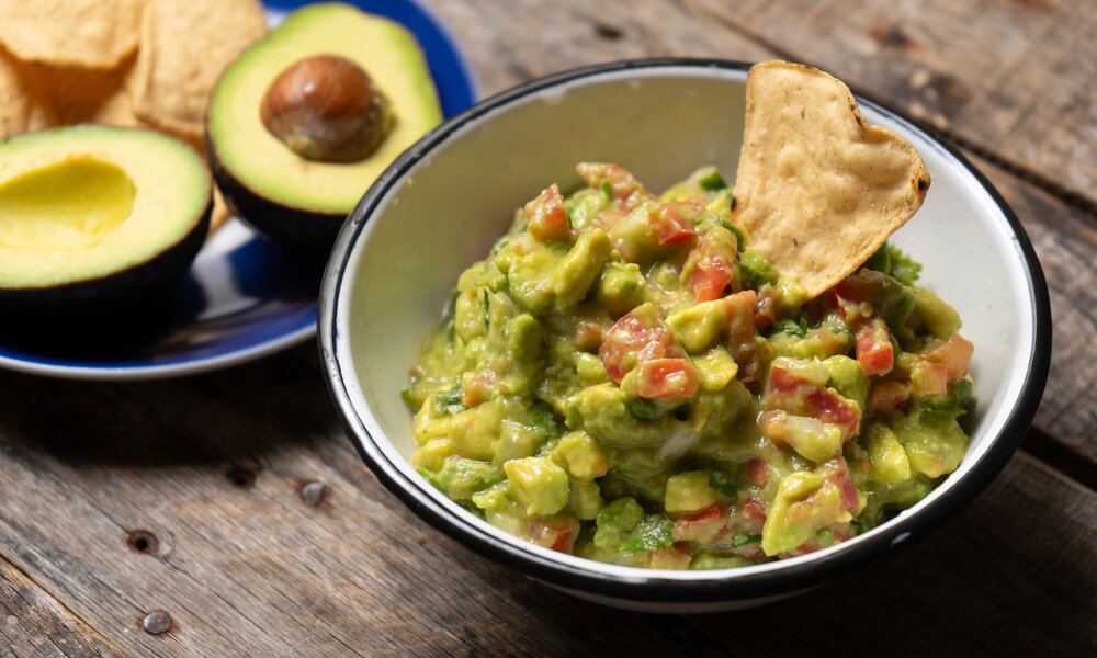 Guacamole angerichtet in Schale, daneben auf Teller aufgeschnittene Avocado und Nachos. | ©  Adobe Stock / Guajillo studio