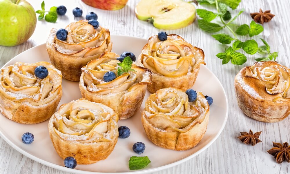 Mehrere Muffins mit Apfelscheiben garniert und frischen Blaubeeren belegt auf einem Teller angerichtet. | © Adobe Stock / myviewpoint