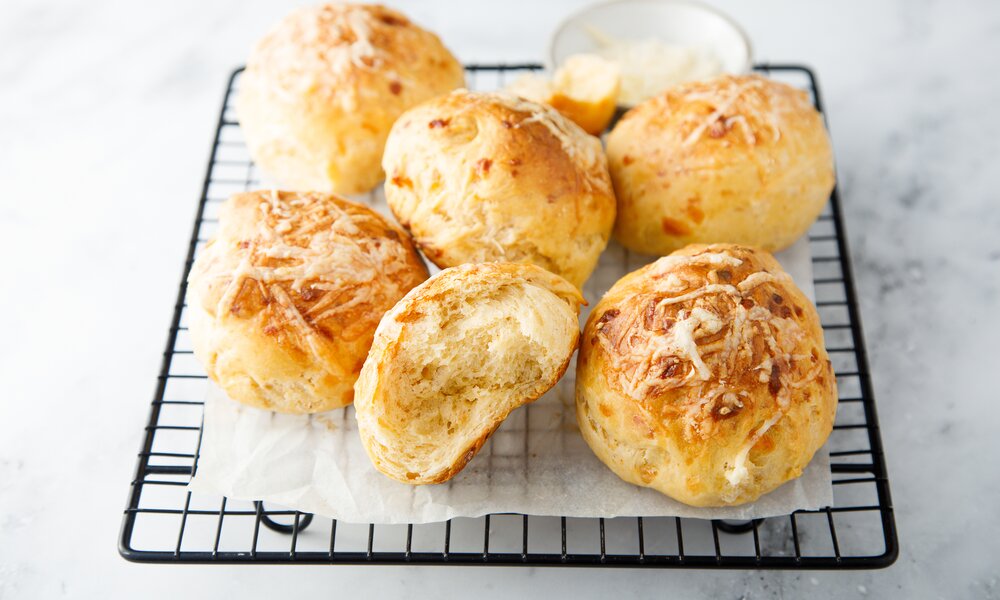 Mehrere auf einem Kuchengitter drapierte Quarkbrötchen mit Käse. | © Adobe Stock / marysckin