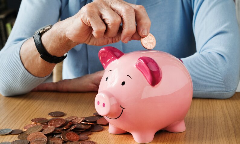Mann legt Münzen in ein Sparschwein | © Getty Images/Image Source