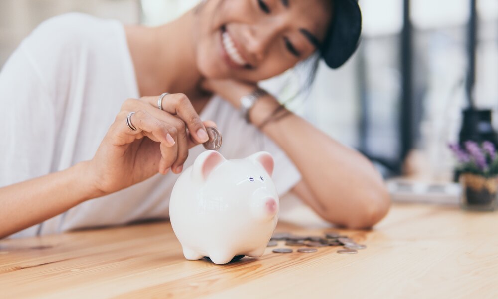 Frau legt Geld in ein Sparschwein | © Getty Images/nomadnes
