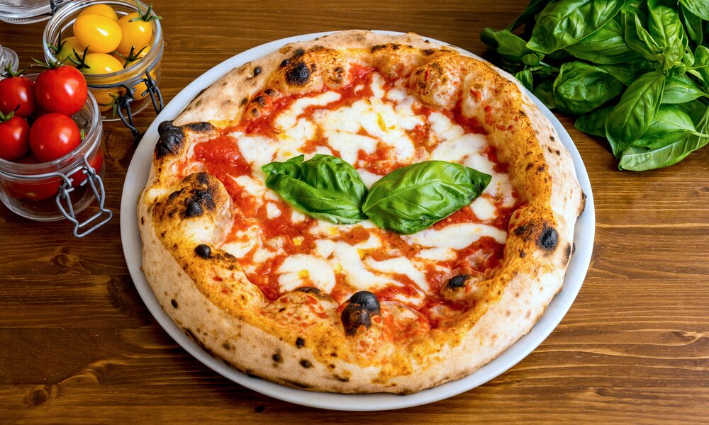Pizza Margaritha auf einem Holzuntergrund daneben frischer Basilikum. | © Getty Images / Photo Beto