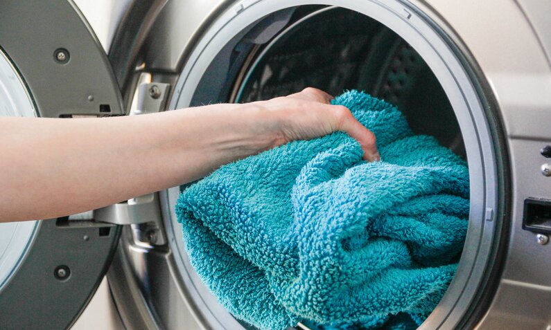 Frau legt Handtuch in Waschmaschine | ©  Getty Images/ 	Kinga Krzeminska