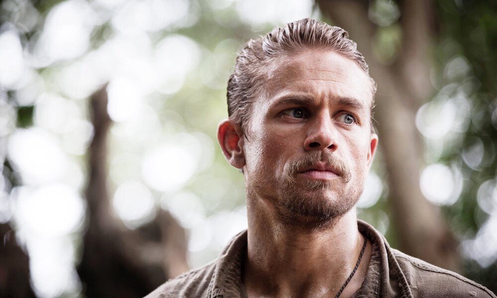 Nahaufnahme von Charlie Hunnam nut Schnurrbart und zurückgegeltem Haar im Wald in einer Szene aus dem Kinofilm "Die versunkene Stadt Z" | © Imago Images/Everett Collection