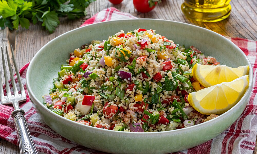Bunter Couscous-Salat in grauer Schüssel, daneben Gabel und Platzdecke. | © Getty Images / BURCU ATALAY TANKUT