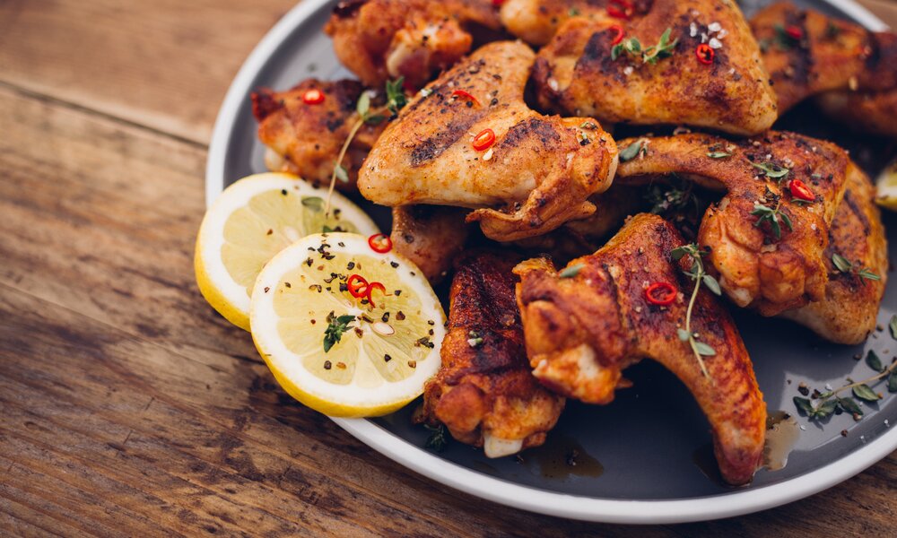 Chicken Wings auf Teller, garniert mit frischer Chili und danebenliegend eine Zitronscheibe. | © Getty Images / 	wundervisuals