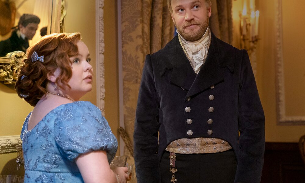 Nicola Coughlan in prächtigem blauen Kleid als Penelope Featherington in einer Szene aus Staffel 3 der Netflix-Serie "Bridgerton" blickt über ihre Schulter - im Hintergrund  Sam Phillips als Lord Debling. | © Netflix /Liam Daniel