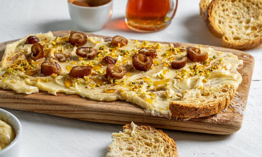 geber Dattel-Dip, wie aus dem Thermomix, ausgestrichen auf einem Holzbrett, darauf garniert einige Stücke getrocknete Datteln. Daneben frische Brotscheiben und etwas Honig in einem Glasbehälter. | © Adobe Stock / TATIANA Z