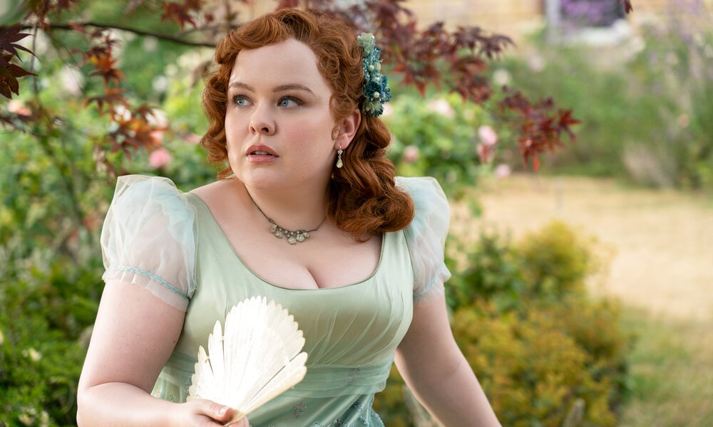 Nicola Coughlan im prächtigen Kleid als Penelope Featherington läuft mit Fächer durch einen Garten in einer Szene der Netflix-Serie "Bridgerton" | © Netflix