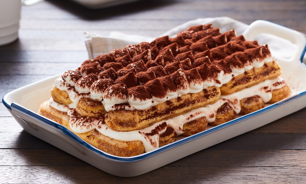 Tiramisu ohne Alkohol angerichtet auf einem Teller, auf einem Holztisch stehend. | © Adobe Stock/ exclusive-design