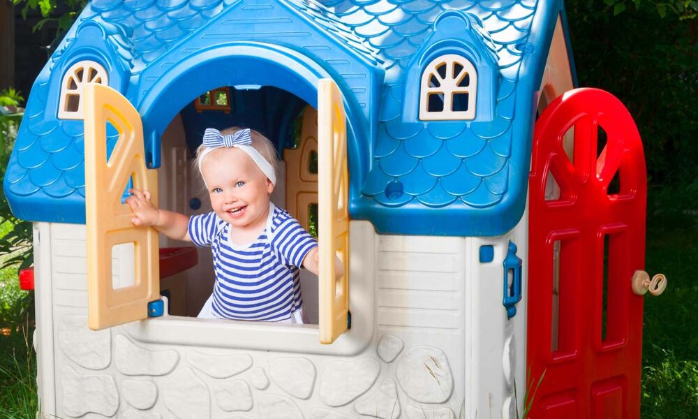 Lachendes Kleinkind mit Haarschleife spielt in buntem Spielhaus im Garten. | © Dmitry Naumov / stock.adobe.com
