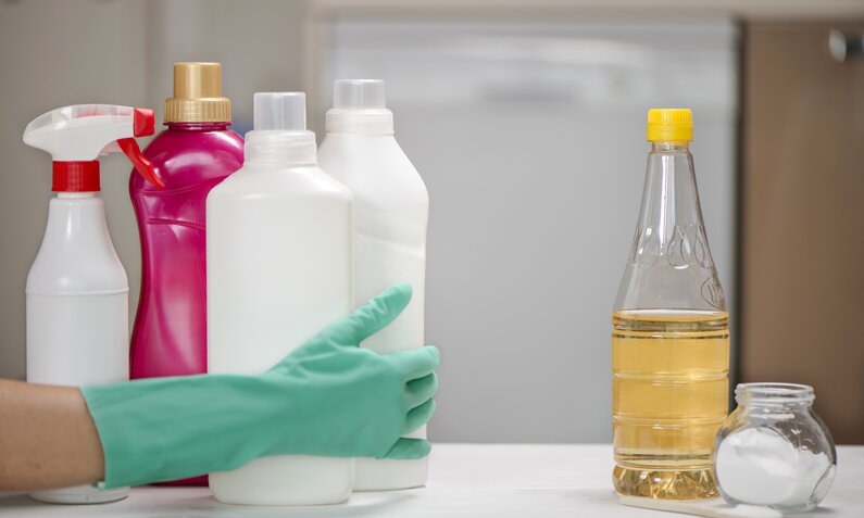 Reinigungsprodukte und Essigflasche auf Küchenarbeitsplatte, Hand in Schutzhandschuh. | © Getty Images/ ozgurkeser