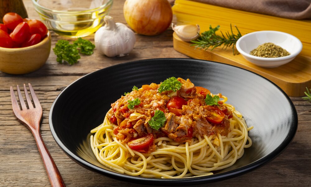 One-Pot-Pasta als Spaghetti mit Thunfisch und Cherrytomaten, angerichtet in einem weißen Suppenteller, garniert mit frischer Petersilie. | © Getty Images / Kritchai Chaibangyang
