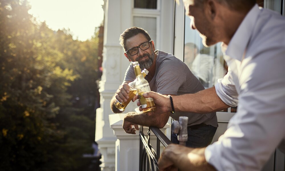 Zwei Männer prosten sich mit Bier auf Balkon zu | © Getty Images/ Oliver Rossi