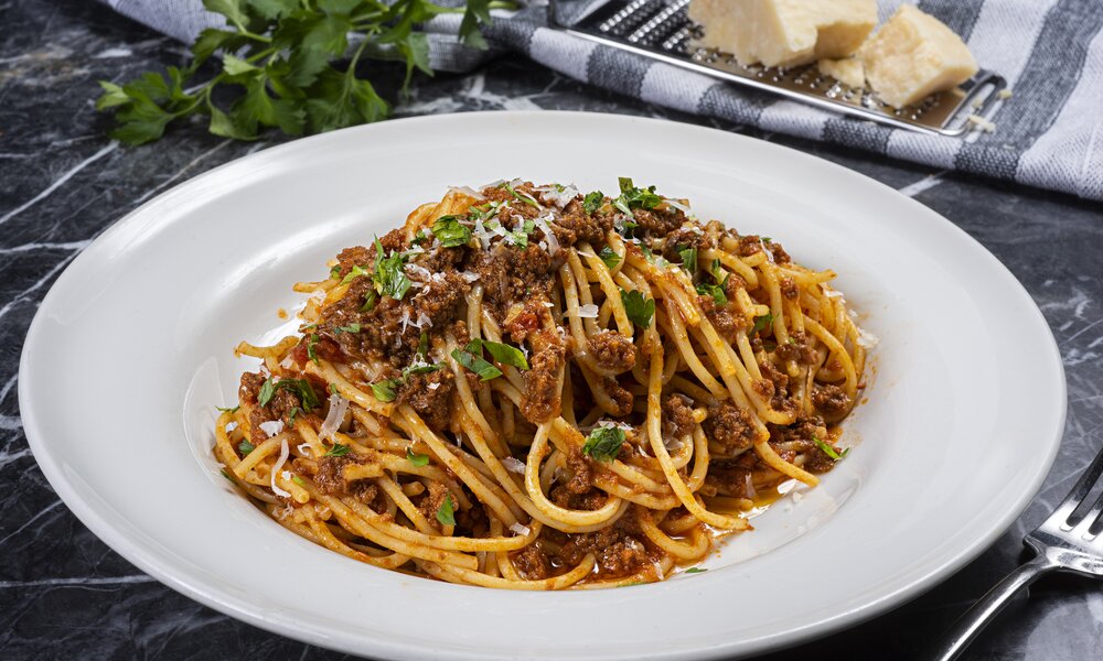 Spaghetti Bolognese in einem weißen Nudelteller auf einem schwarzen Marmoruntergrund angerichtet. | © Getty Images / BURCU ATALAY TANKUT