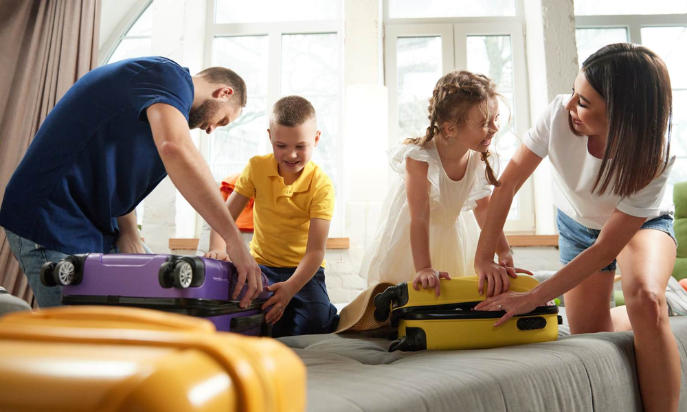 Glückliche Eltern und Kinder beim Packen, umgeben von gelbem und lila Koffer im Wohnzimmer. | © master1305/stock.adobe.com