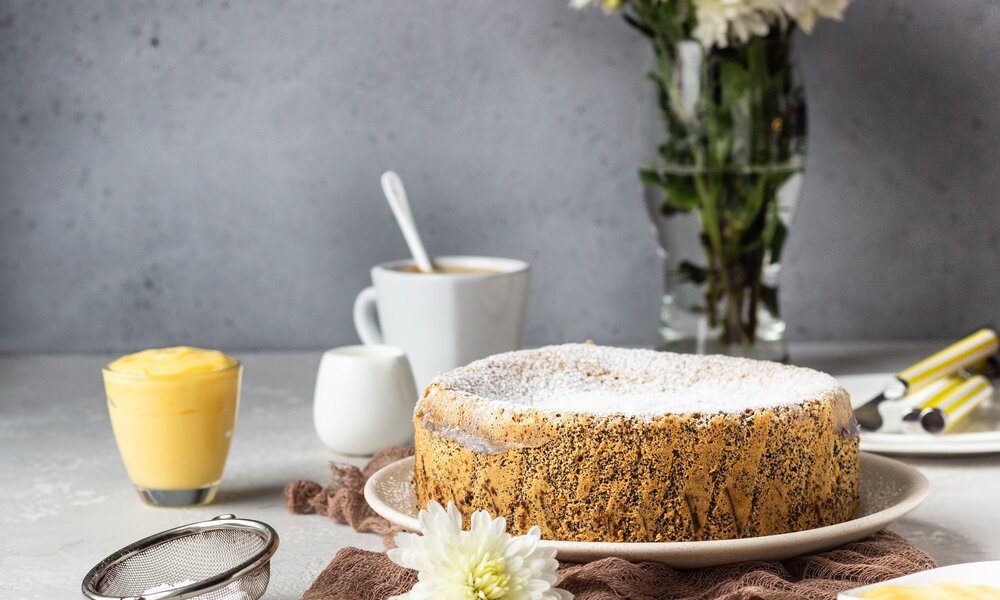 Mohnkuchen mit Puddingfüllung angerichtet auf Tortenplatte, garniert mit Blüten, daneben Pudding in Behälter. | © Getty Images / 	porosolka