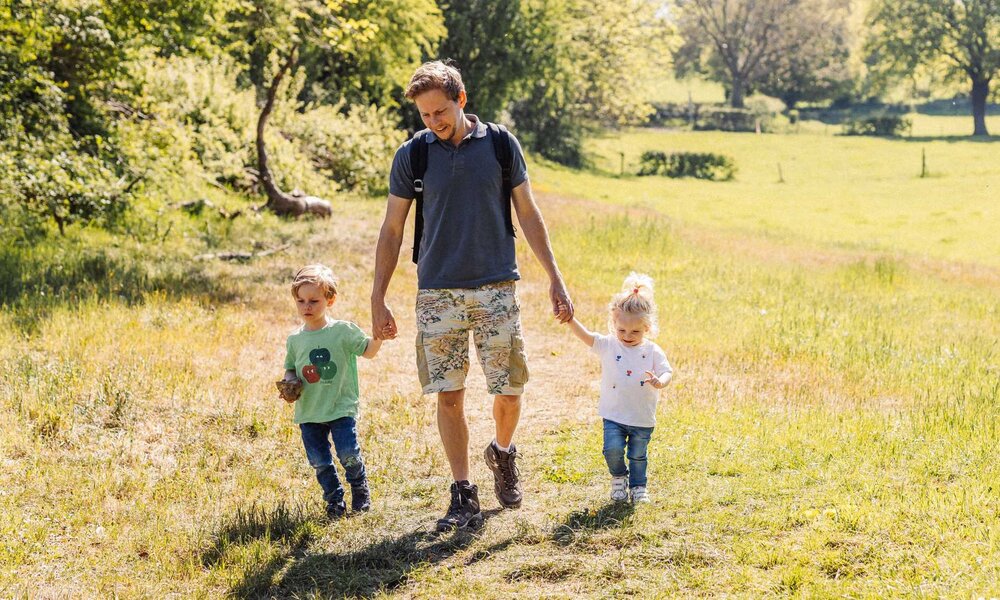 Vater geht mit zwei Kindern bei sonnigem Wetter auf einem Feldweg spazieren.  | © Julien/stock.adobe.com